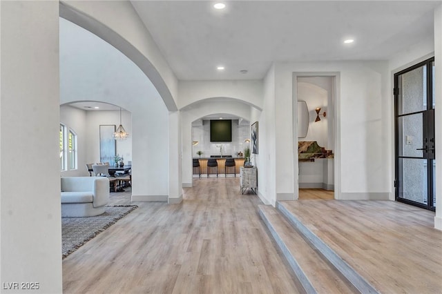 foyer with light wood-style flooring, arched walkways, and baseboards