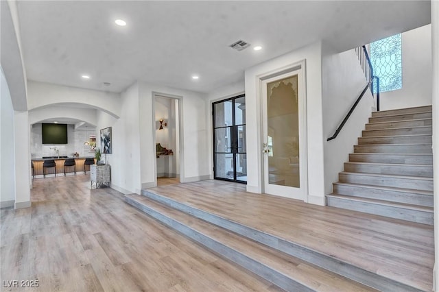 entryway featuring light wood finished floors, visible vents, arched walkways, stairway, and recessed lighting