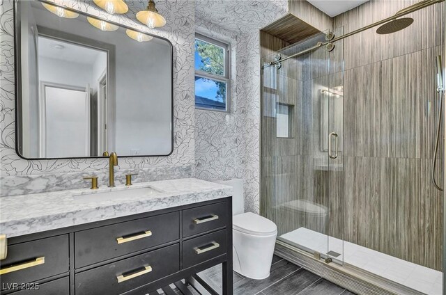 bathroom featuring toilet, a stall shower, vanity, and wallpapered walls