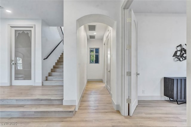 hallway with light wood-type flooring, visible vents, arched walkways, and baseboards