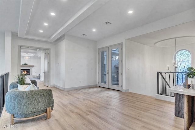 living area featuring french doors, a notable chandelier, recessed lighting, light wood-type flooring, and a warm lit fireplace