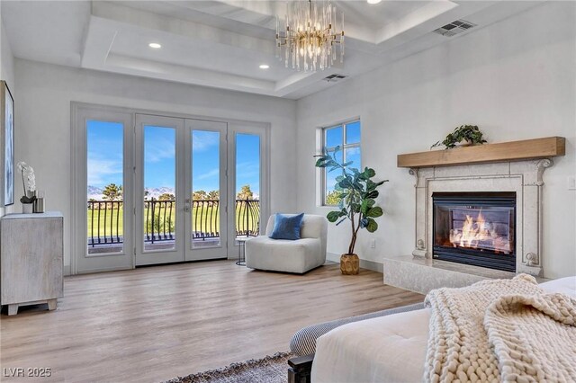 living area with a raised ceiling, a premium fireplace, a chandelier, and light wood-type flooring