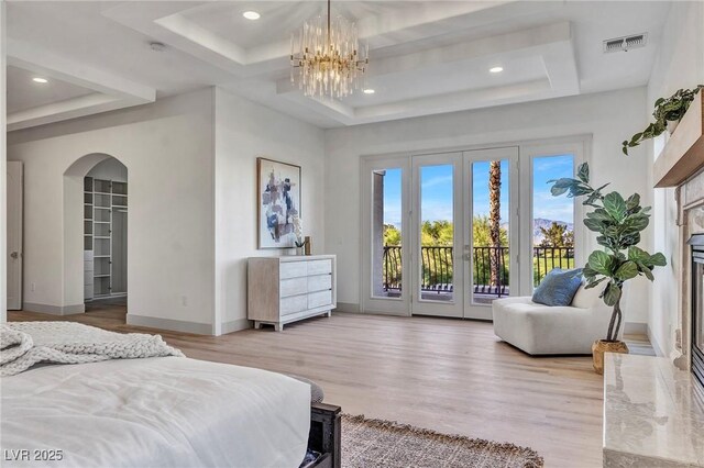 bedroom with a tray ceiling, a high end fireplace, access to outside, and light wood-type flooring