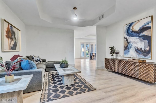 living room featuring baseboards, a tray ceiling, visible vents, and light wood-style floors