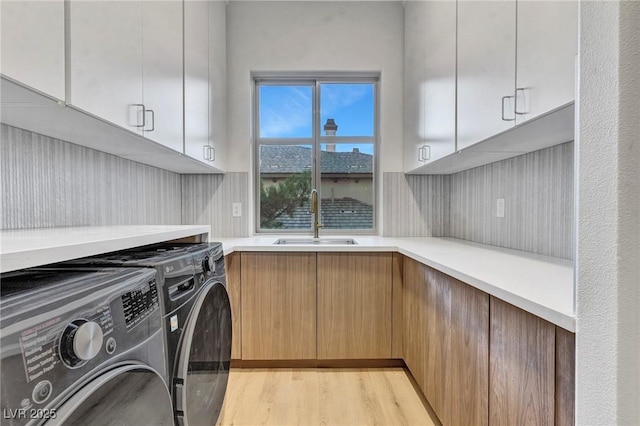 clothes washing area featuring cabinet space, washing machine and dryer, and a sink