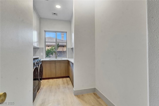 clothes washing area with cabinets, independent washer and dryer, and light hardwood / wood-style flooring