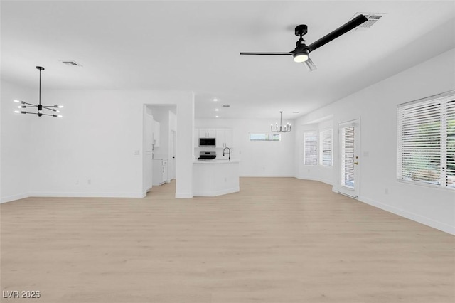 unfurnished living room featuring sink, ceiling fan with notable chandelier, plenty of natural light, and light wood-type flooring