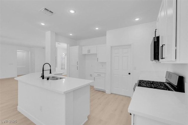 kitchen with sink, gas range, a center island with sink, light hardwood / wood-style floors, and white cabinets