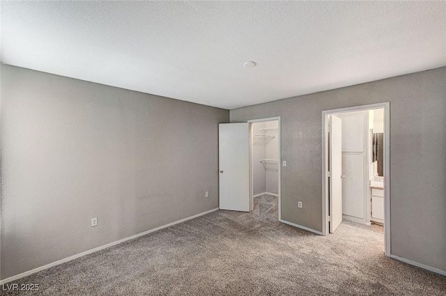 unfurnished bedroom featuring connected bathroom, a spacious closet, light colored carpet, a textured ceiling, and a closet