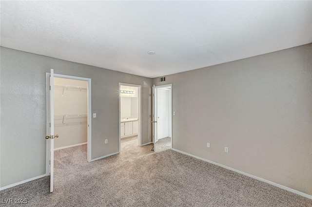 unfurnished bedroom featuring light colored carpet, ensuite bathroom, a spacious closet, and a closet