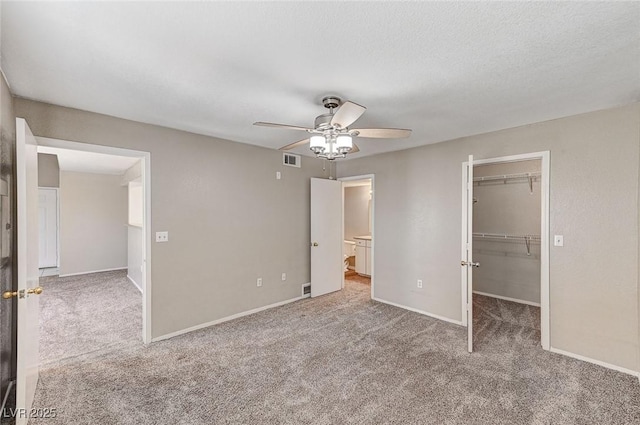 unfurnished bedroom featuring ceiling fan, a textured ceiling, light carpet, a spacious closet, and a closet