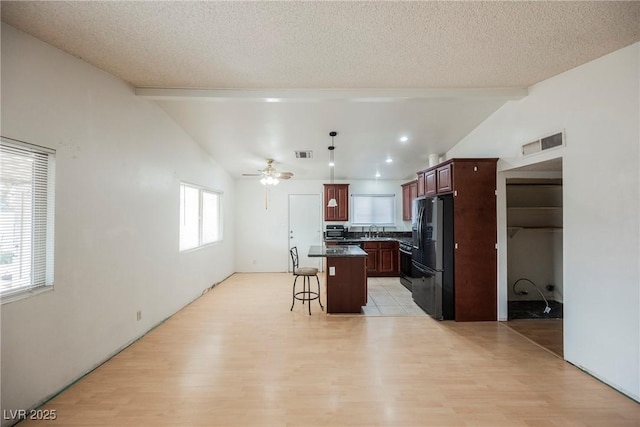 kitchen featuring a kitchen island, black refrigerator, a breakfast bar, sink, and vaulted ceiling with beams