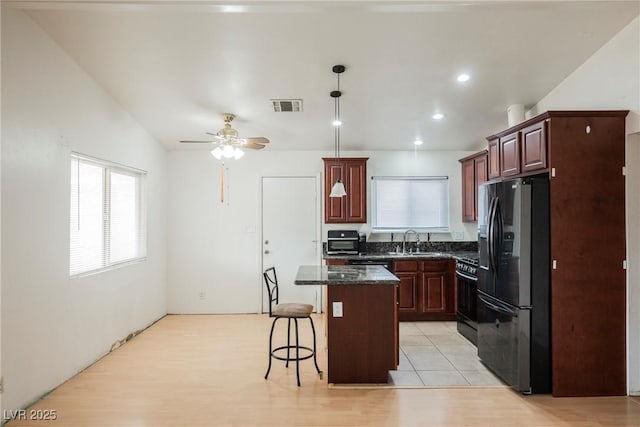 kitchen with sink, gas range oven, a kitchen island, black fridge with ice dispenser, and dark stone counters