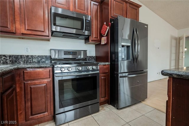 kitchen with stainless steel appliances, light tile patterned floors, a textured ceiling, and dark stone counters