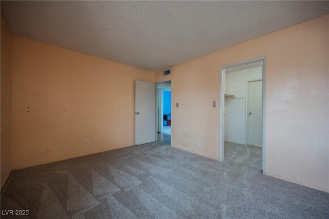 unfurnished bedroom featuring a spacious closet, light carpet, and a textured ceiling