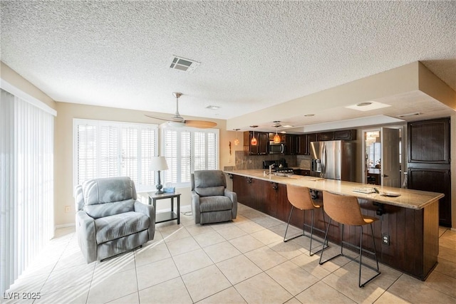 kitchen with dark brown cabinetry, light tile patterned floors, a kitchen breakfast bar, kitchen peninsula, and stainless steel appliances