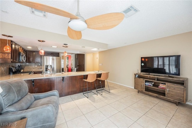 kitchen with a kitchen bar, hanging light fixtures, dark brown cabinets, kitchen peninsula, and stainless steel appliances