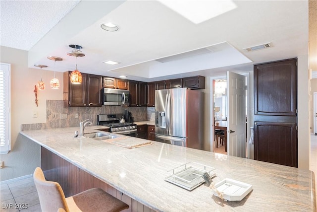 kitchen with decorative light fixtures, dark brown cabinets, kitchen peninsula, stainless steel appliances, and decorative backsplash