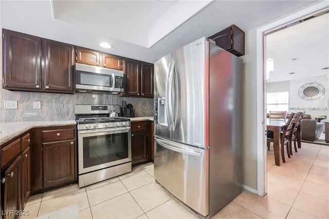 kitchen with appliances with stainless steel finishes, a tray ceiling, light tile patterned floors, and backsplash