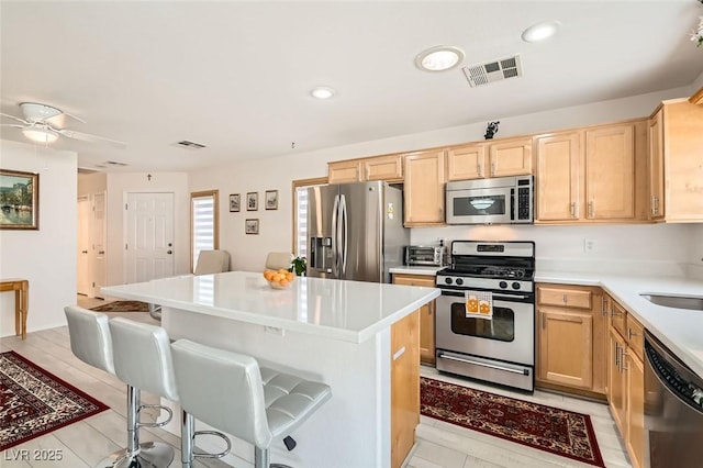 kitchen with a breakfast bar, sink, a center island, stainless steel appliances, and light brown cabinets