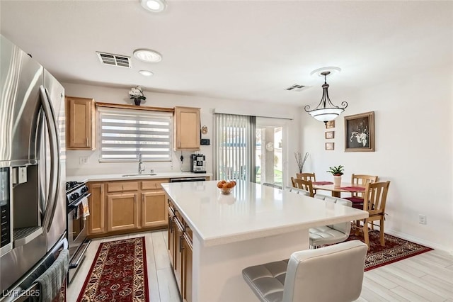 kitchen with sink, range, hanging light fixtures, stainless steel fridge, and a kitchen island