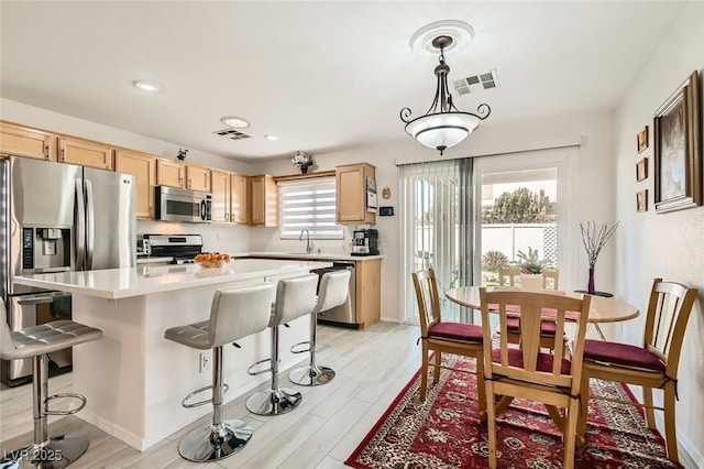 kitchen featuring appliances with stainless steel finishes, light brown cabinetry, decorative light fixtures, sink, and a center island