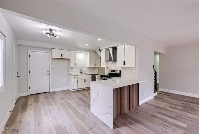 kitchen with light wood-type flooring, stainless steel range, kitchen peninsula, white cabinets, and wall chimney range hood