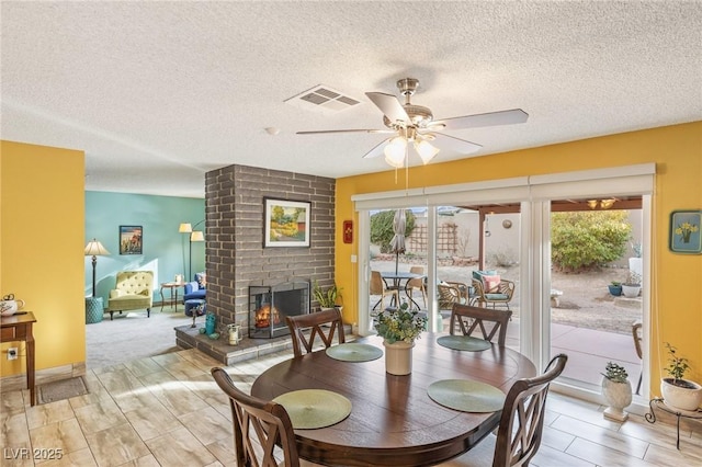 dining room with a brick fireplace, a textured ceiling, and ceiling fan