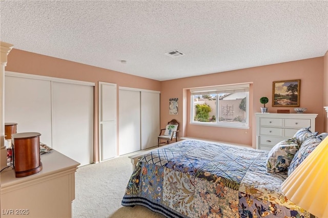 bedroom featuring multiple closets, carpet floors, a textured ceiling, and ornate columns