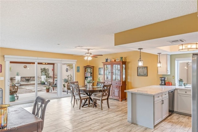 kitchen with light stone counters, hanging light fixtures, appliances with stainless steel finishes, kitchen peninsula, and light hardwood / wood-style floors