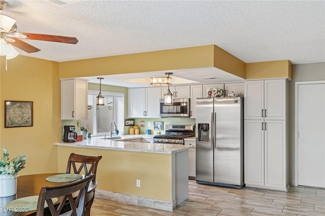 kitchen with appliances with stainless steel finishes, pendant lighting, sink, white cabinets, and kitchen peninsula