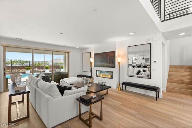 living room featuring light wood-style flooring, recessed lighting, visible vents, stairway, and a glass covered fireplace