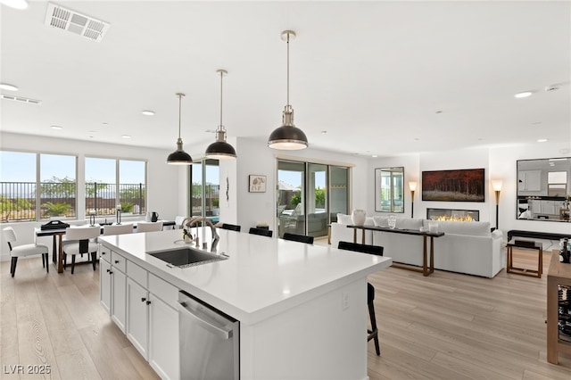 kitchen with sink, decorative light fixtures, stainless steel dishwasher, an island with sink, and white cabinets