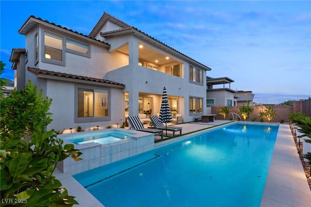 rear view of house with a fenced in pool, a tiled roof, an in ground hot tub, fence, and stucco siding