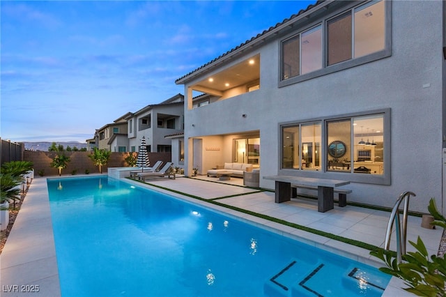 pool at dusk with an outdoor hangout area, a patio, fence, and a fenced in pool