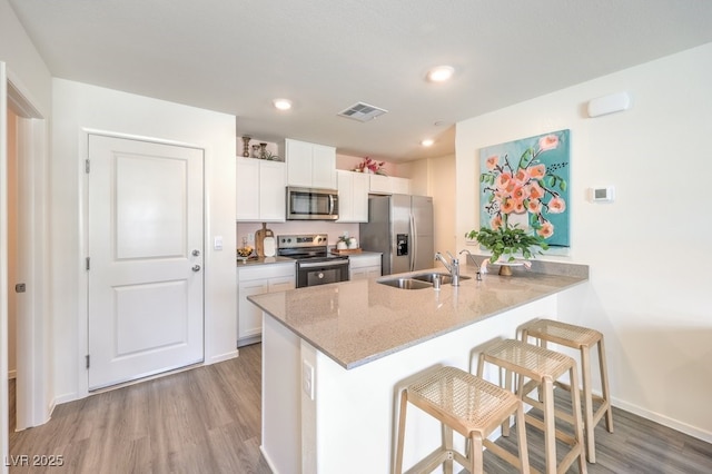 kitchen with sink, a breakfast bar, appliances with stainless steel finishes, white cabinets, and kitchen peninsula