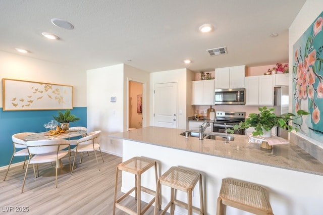 kitchen with sink, white cabinetry, light hardwood / wood-style flooring, kitchen peninsula, and stainless steel appliances