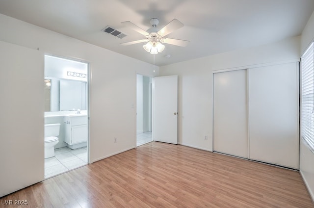 unfurnished bedroom with ensuite bathroom, sink, light hardwood / wood-style flooring, ceiling fan, and a closet