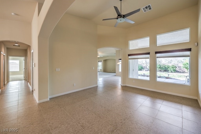 spare room featuring ceiling fan, light tile patterned floors, a healthy amount of sunlight, and a high ceiling