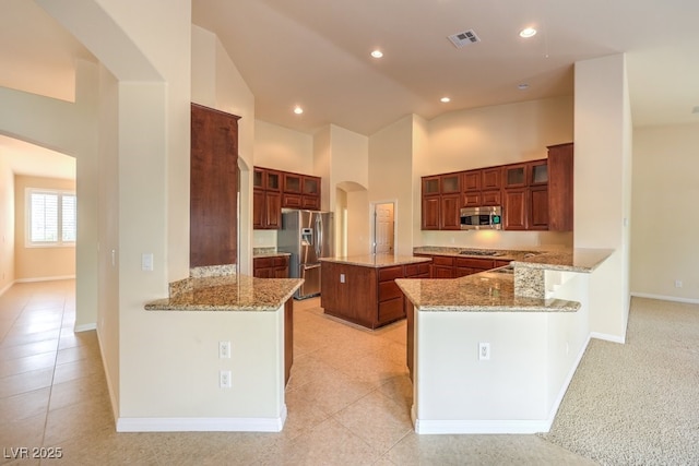 kitchen featuring a kitchen island, appliances with stainless steel finishes, high vaulted ceiling, kitchen peninsula, and light stone countertops