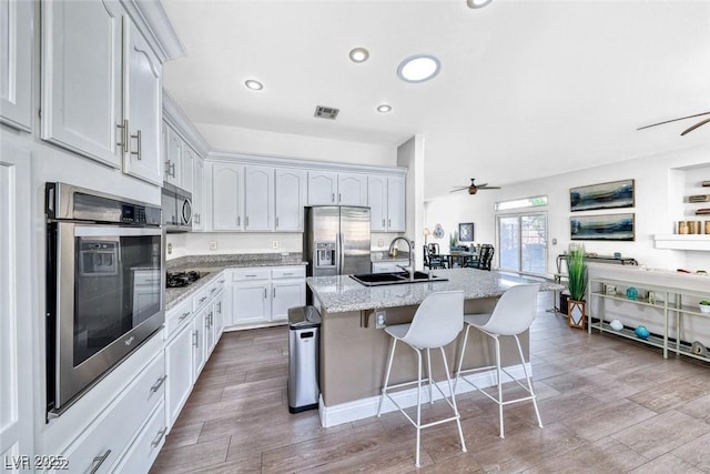 kitchen featuring white cabinetry, sink, stainless steel appliances, light stone countertops, and a center island with sink