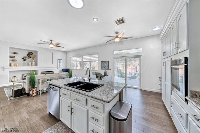 kitchen featuring appliances with stainless steel finishes, sink, white cabinets, a kitchen island with sink, and light stone countertops