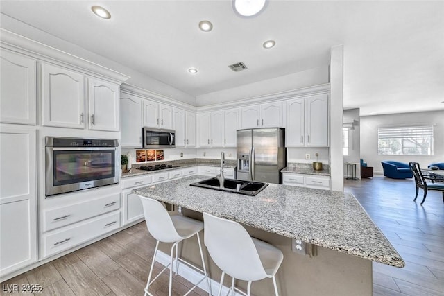 kitchen featuring appliances with stainless steel finishes, sink, white cabinets, light stone counters, and light wood-type flooring