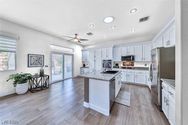 kitchen with stainless steel appliances, light stone countertops, a kitchen island with sink, and white cabinets