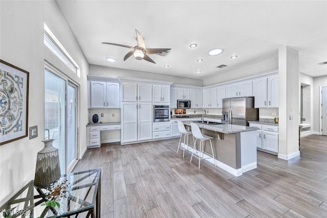 kitchen featuring a breakfast bar area, stainless steel appliances, light stone countertops, white cabinets, and a center island with sink