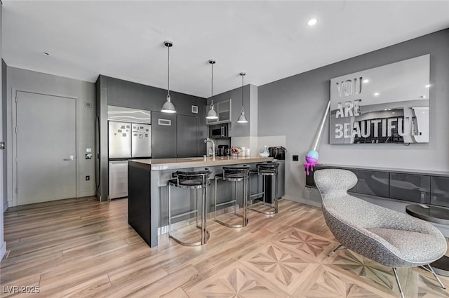 kitchen with appliances with stainless steel finishes, decorative light fixtures, a breakfast bar area, kitchen peninsula, and light hardwood / wood-style flooring