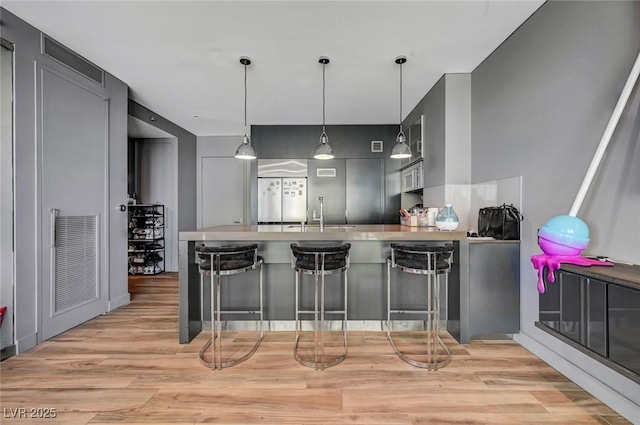 kitchen with gray cabinets, a breakfast bar, hanging light fixtures, kitchen peninsula, and light hardwood / wood-style flooring