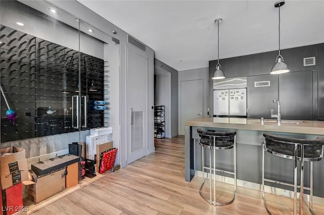 kitchen with pendant lighting, fridge, sink, and light wood-type flooring