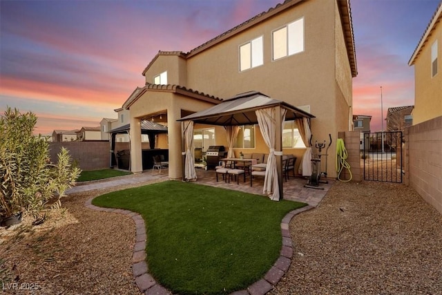 back house at dusk featuring a gazebo, a lawn, and a patio