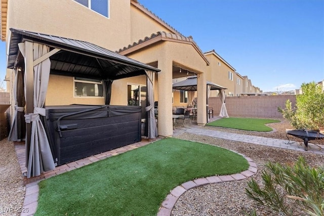 back of property featuring a gazebo, a patio, a hot tub, and a lawn